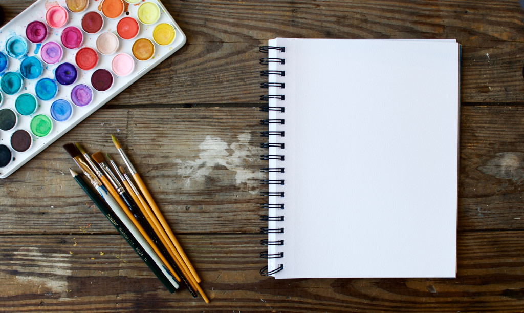 A blank notepad and watercolor paints and brushes